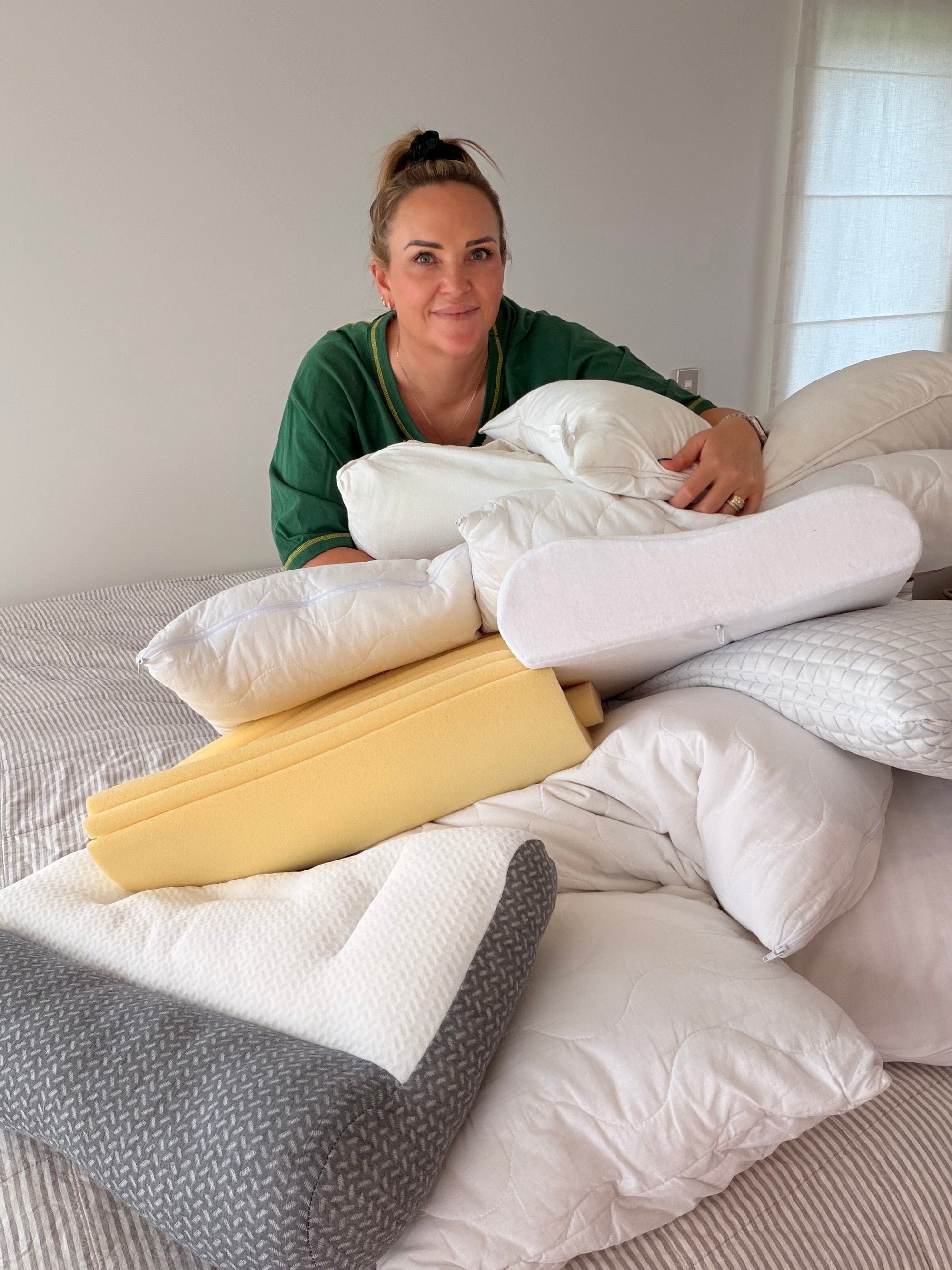 A woman surrounded by various contour and orthopaedic pillows on a bed, illustrating the process of testing the best sleep products for the 2026 Dream Sleep, Ecosa, and TEMPUR comparison guide in New Zealand