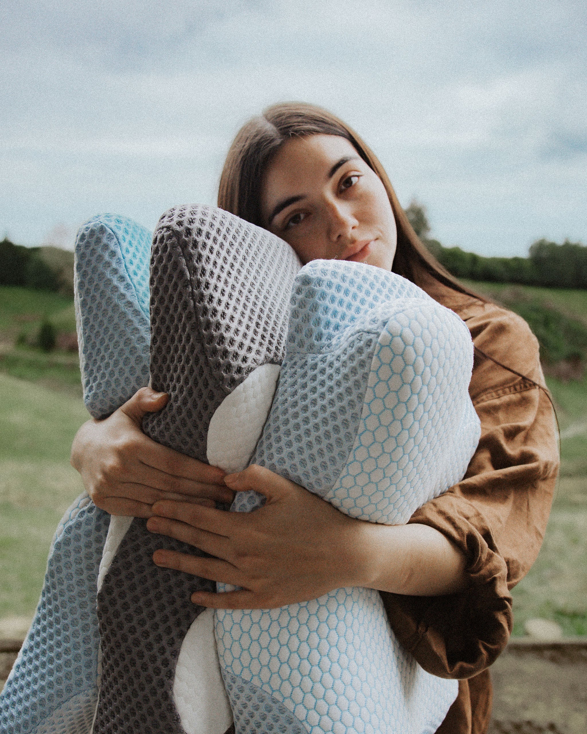 Woman holding a large, textured pillow outdoors with a natural background