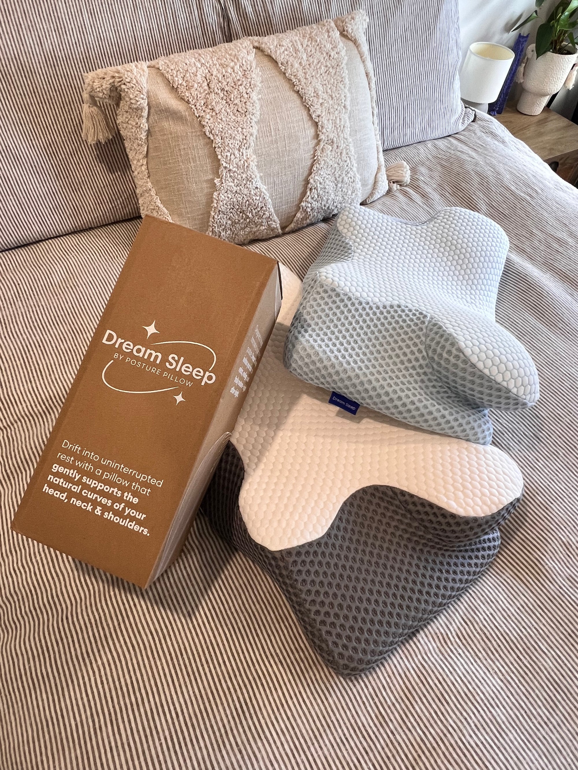 A display of Dream Sleep orthopaedic pillows with various textures on a bed next to the branded product packaging.