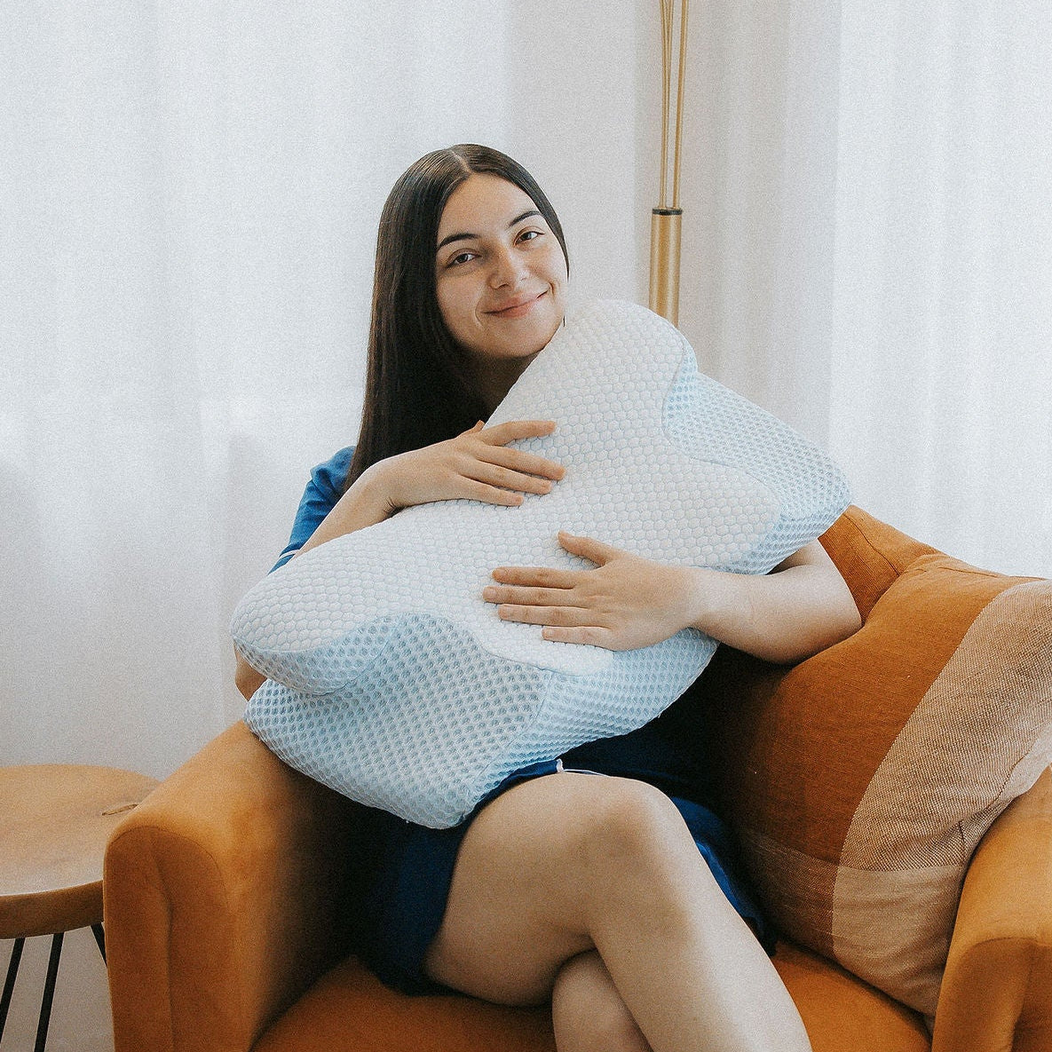 Close-up of the Alpine Blue Dream Sleep posture pillow being held by a woman in a bright, comfortable room.