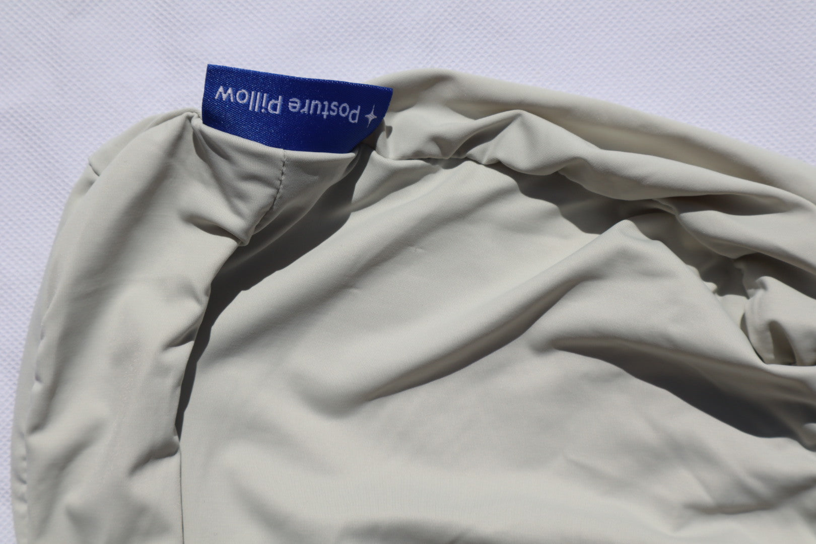 Close-up of the Posture Pillow with the branded label, showing the smooth, light fabric cover for comfortable spinal alignment.