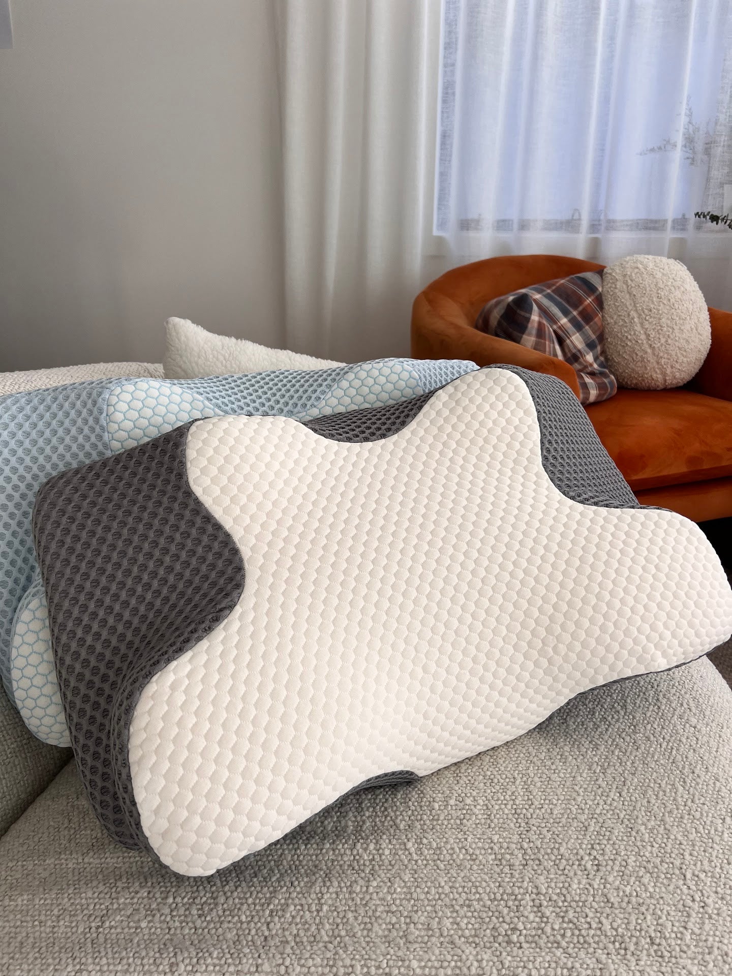 Lifestyle shot of the Signature Twin Pillow Set in Alpine Blue and Cloud Grey, showing the unique ergonomic contour shape on a living room sofa.